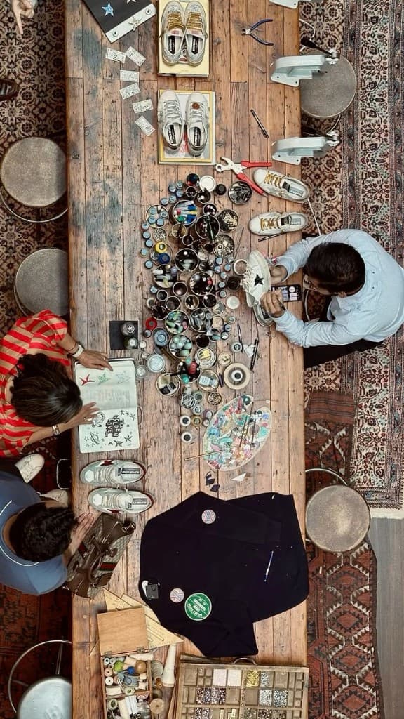 Overhead view of a Golden Goose work table, with shoes, paint, and people customizing by hand