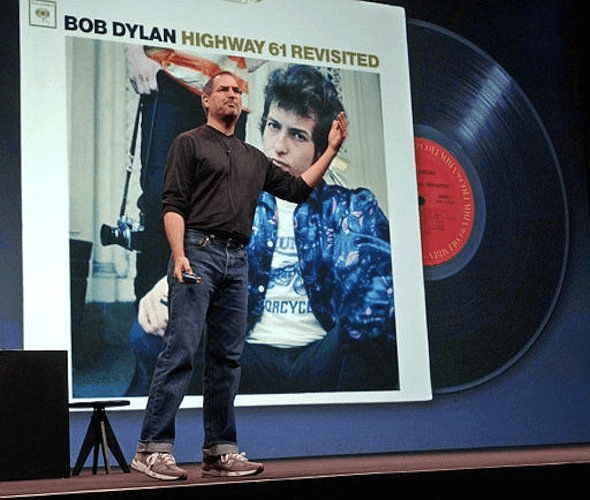 Steve Jobs on stage beside the Bob Dylan Highway 61 Revisited cover during an Apple presentation