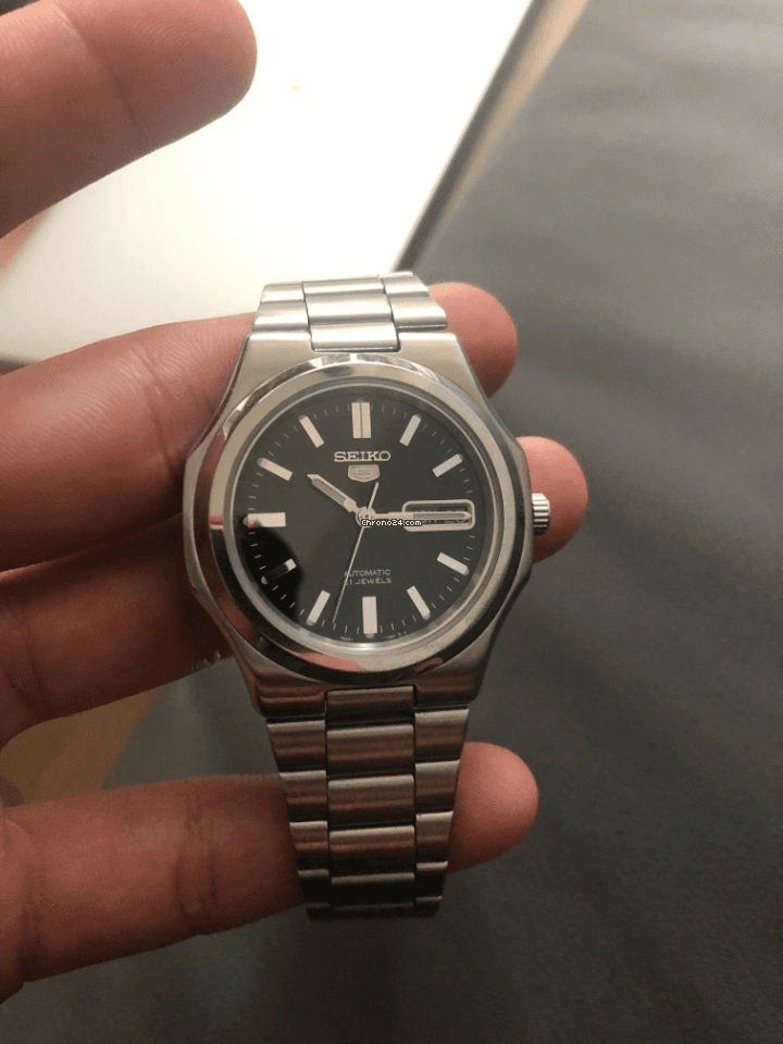 A Seiko on a metal bracelet, held in the hand, with a black dial and thick stick indices